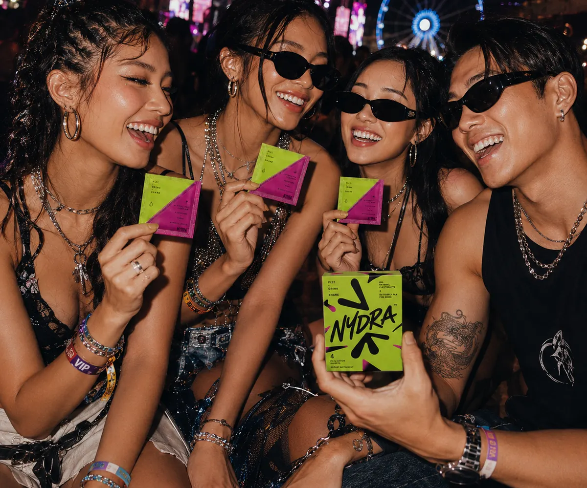 Four friends at a festival holding NYDRA sachets and the box